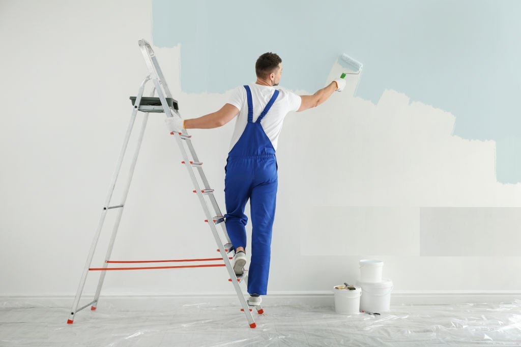 Man painting wall with light blue dye indoors, back view